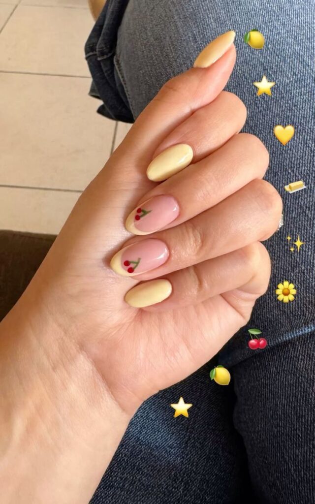 Butter yellow almond nails with cherry designs on two negative space accent nails.