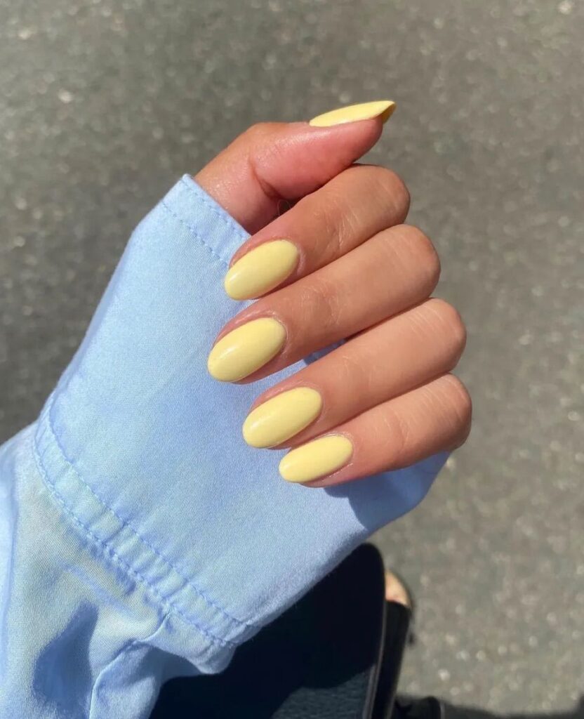 Rounded butter yellow nails peeking out from a light blue shirt cuff in sunlight.