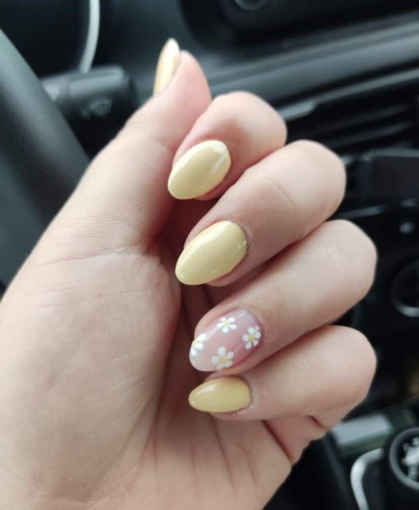 Butter yellow almond nails with a pink accent nail covered in white daisies.