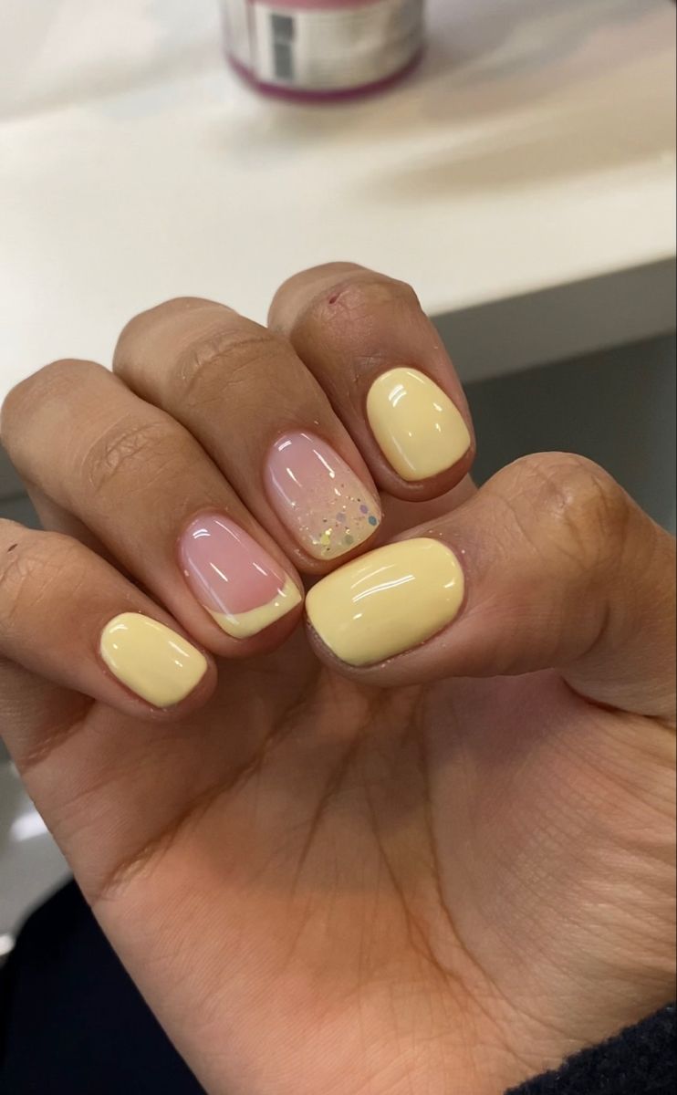 Short butter yellow nails mixing solid colour, a French tip and a glitter accent