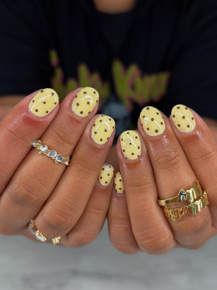 Short butter yellow nails with scattered brown dots creating a cookie style pattern.