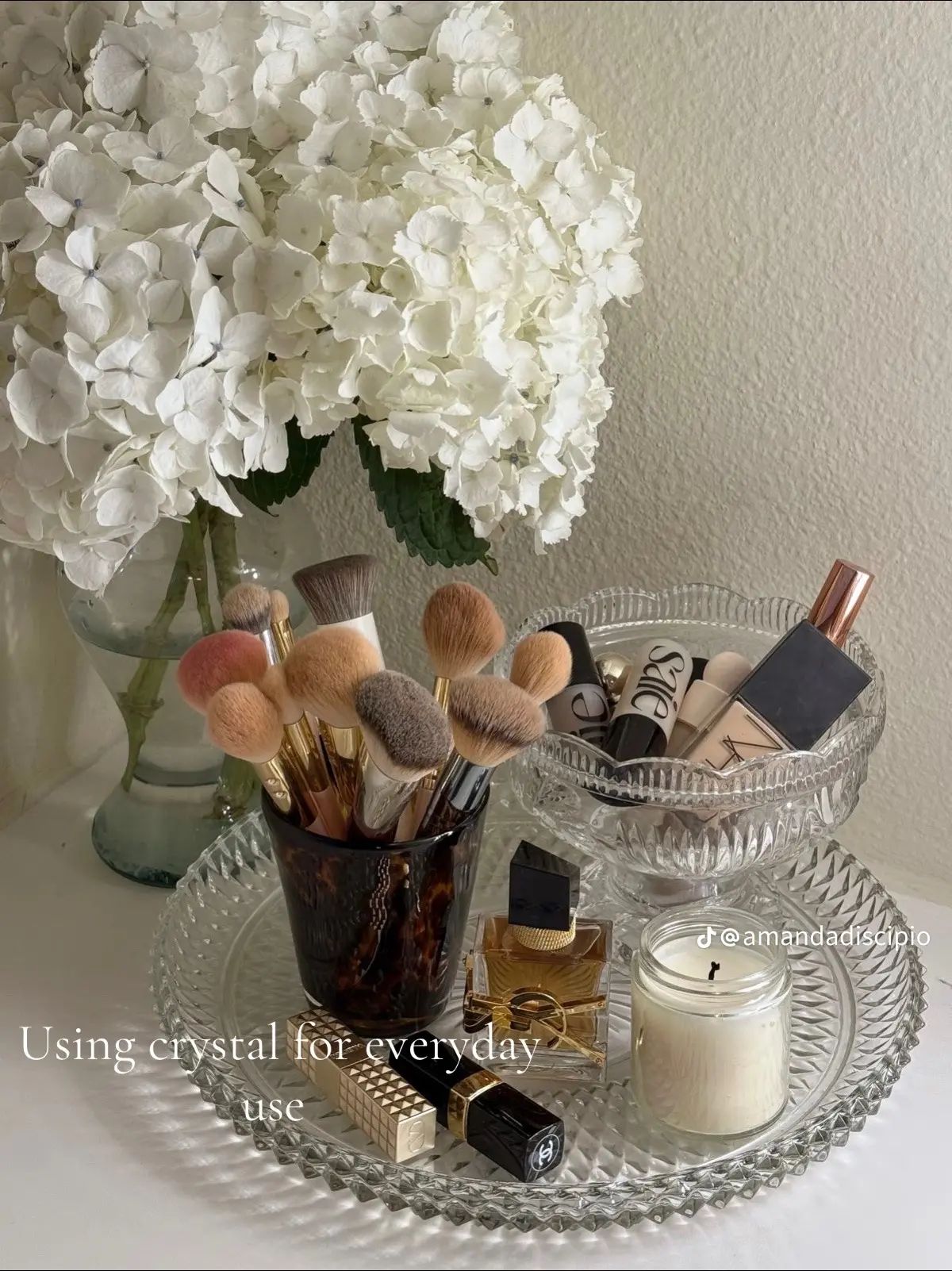 Crystal tray styled with makeup brushes, candle, perfume and white hydrangeas on a bathroom counter