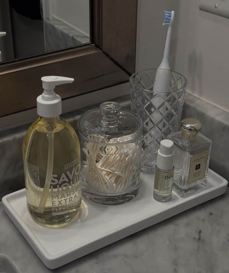 White stone tray with hand wash, cotton bud jar and perfume on a marble bathroom counter