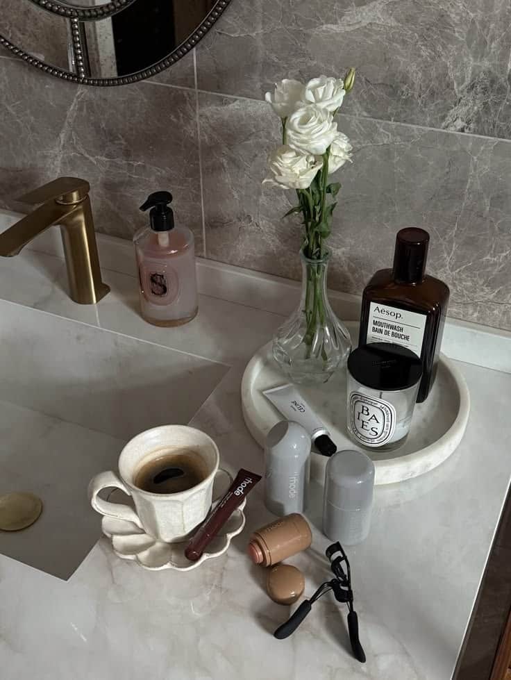 Marble bathroom counter with skincare tray, white roses in a vase, coffee cup and beauty products
