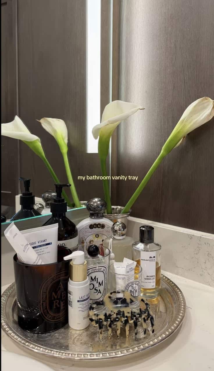 Round silver vanity tray with calla lilies, Diptyque candle, serums and designer perfume bottles