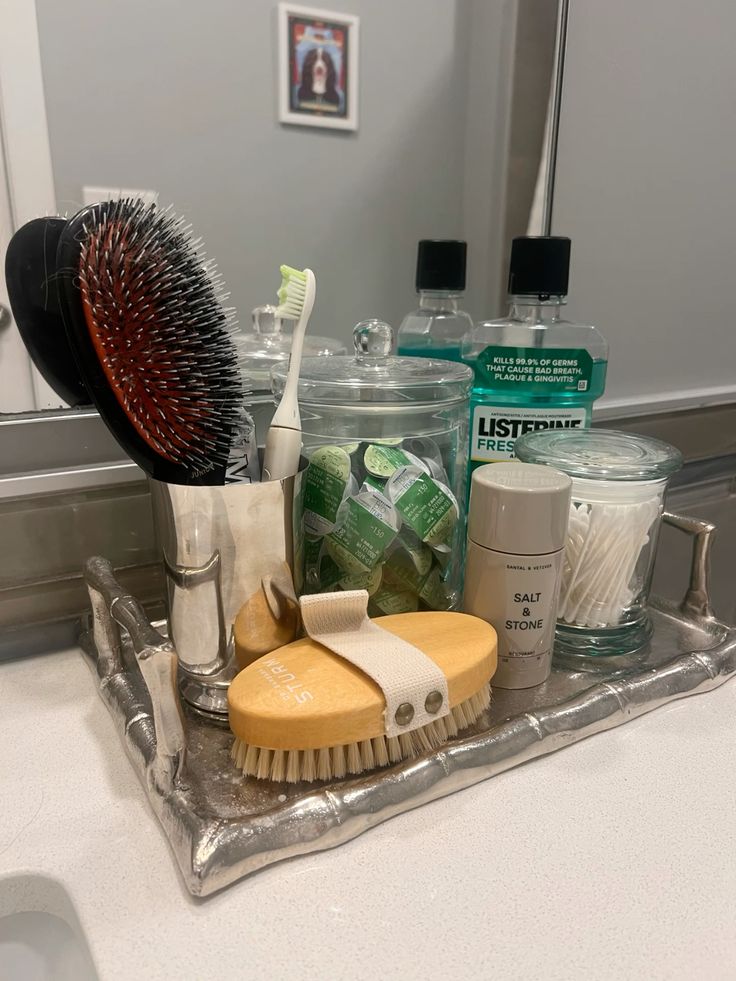 Decorative silver tray holding a hair brush, dry brush, deodorant and cotton buds on a bathroom counter