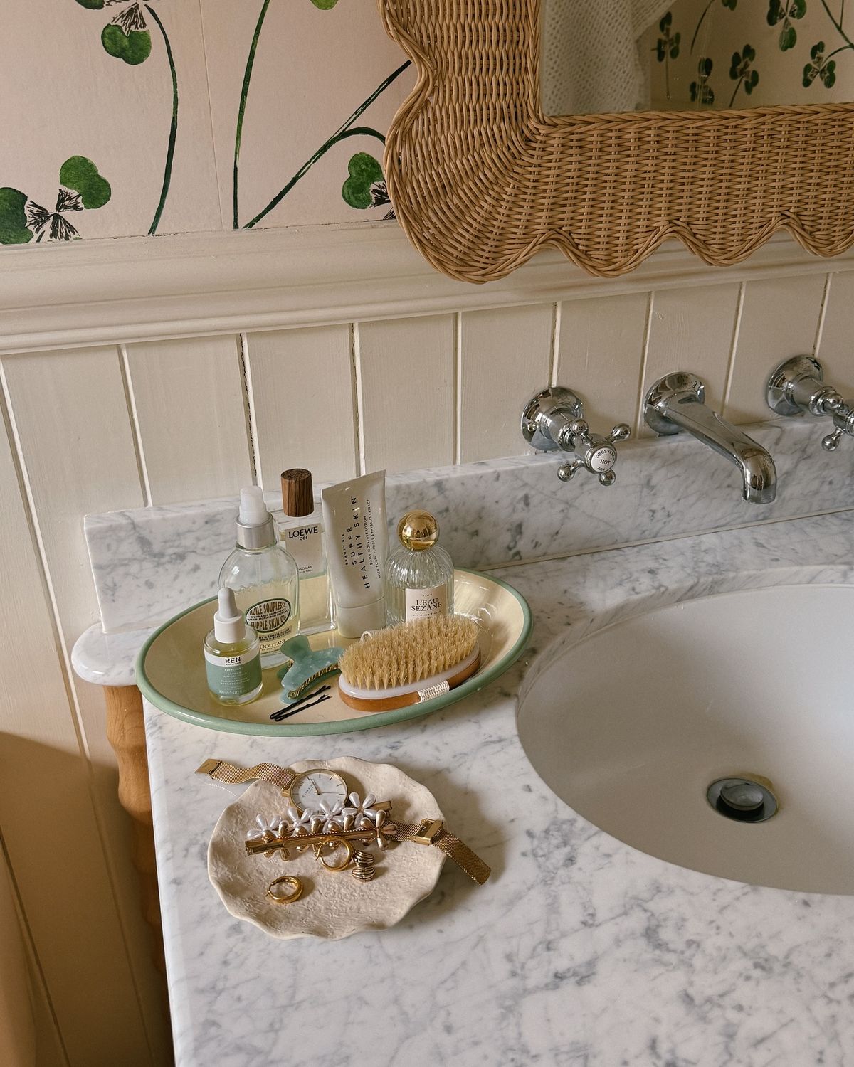 Sage green oval tray with skincare products, face brush and a small handmade jewellery dish on a marble counter