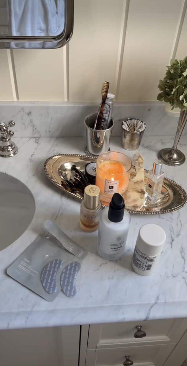 Silver oval tray with candle, hair combs, perfume and serums on a marble bathroom counter