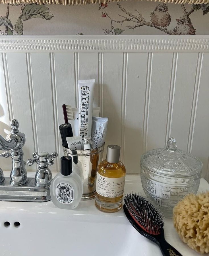 Silver cup holding toothbrush and toothpaste next to a Diptyque perfume and a candle on a bathroom counter