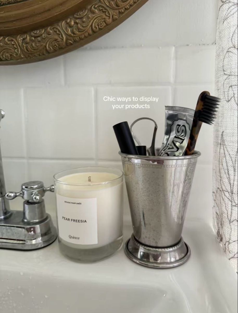 Mint julep silver cup with toothbrush and toothpaste next to a white candle on a bathroom counter