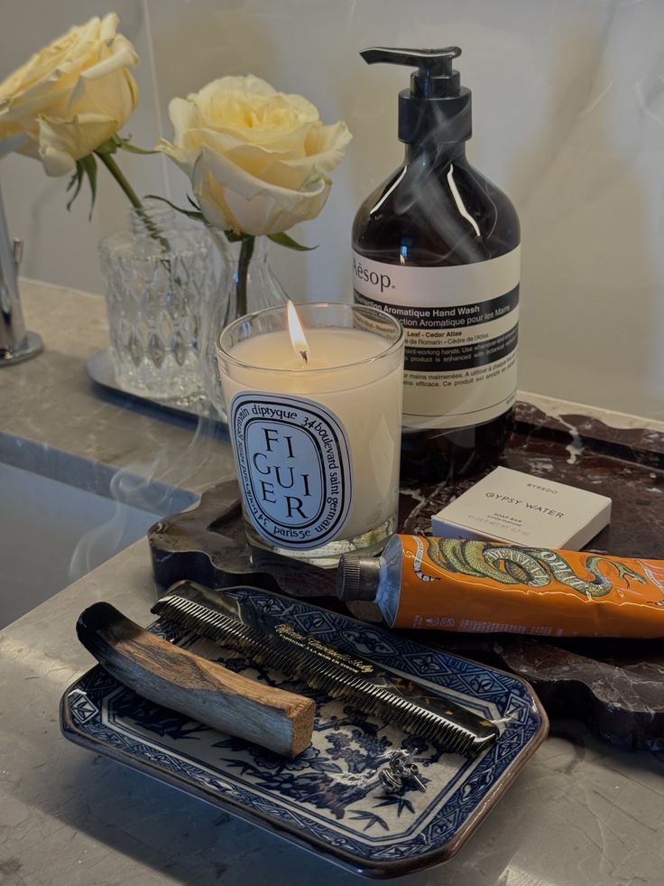 Diptyque candle, Aesop hand wash and a blue and white trinket dish styled on a dark marble bathroom counter