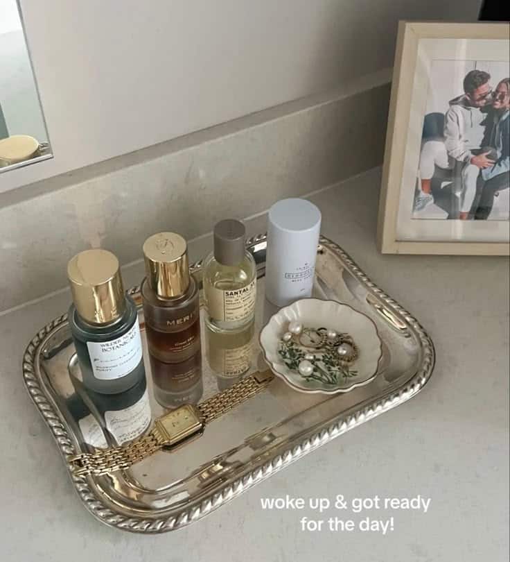 Silver vanity tray with perfume bottles, gold watch and a small jewellery dish on a bathroom counter