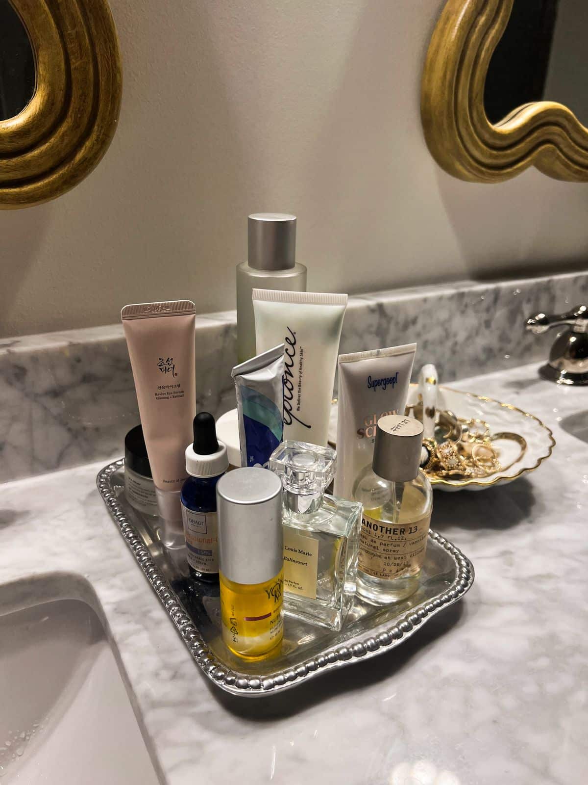 Beaded silver tray with skincare serums and a scalloped jewellery dish on a marble bathroom counter