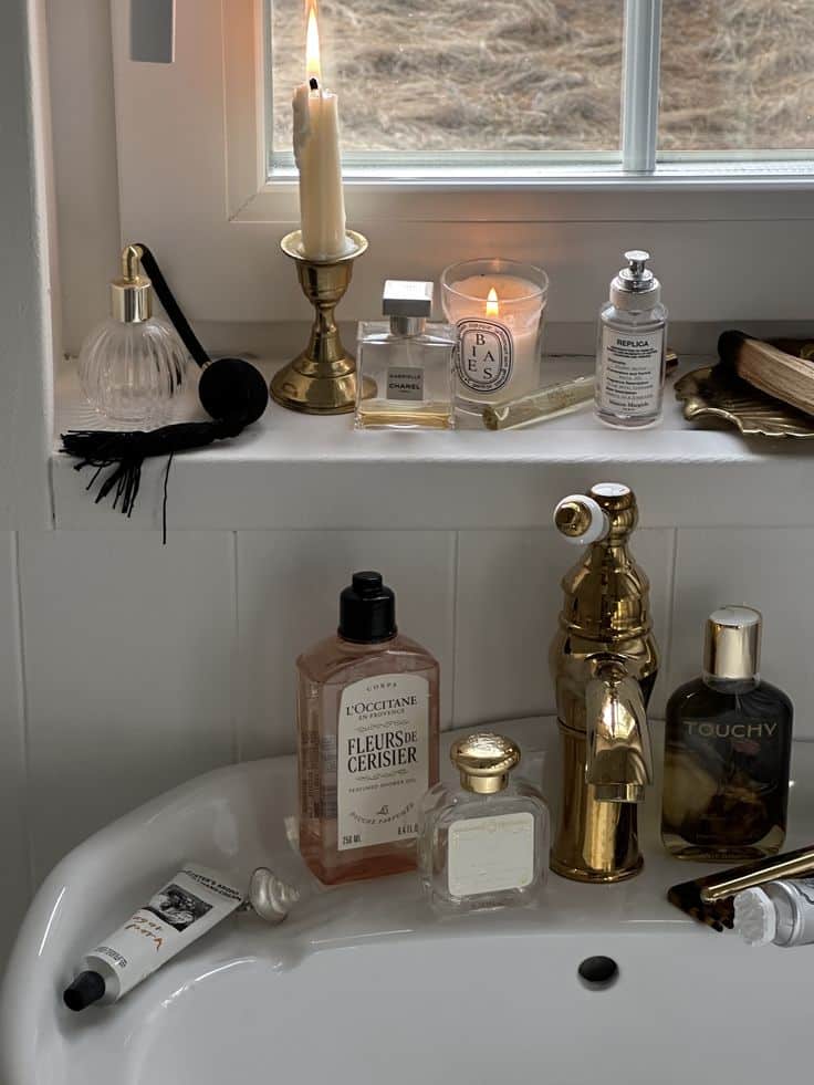 Bathroom window ledge styled with brass candlestick, lit candles and designer perfume bottles