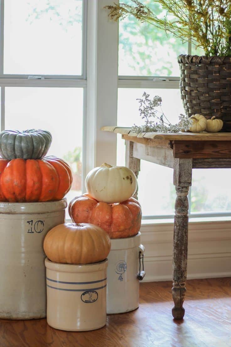 Heirloom pumpkins stacked on vintage stoneware crocks by a window