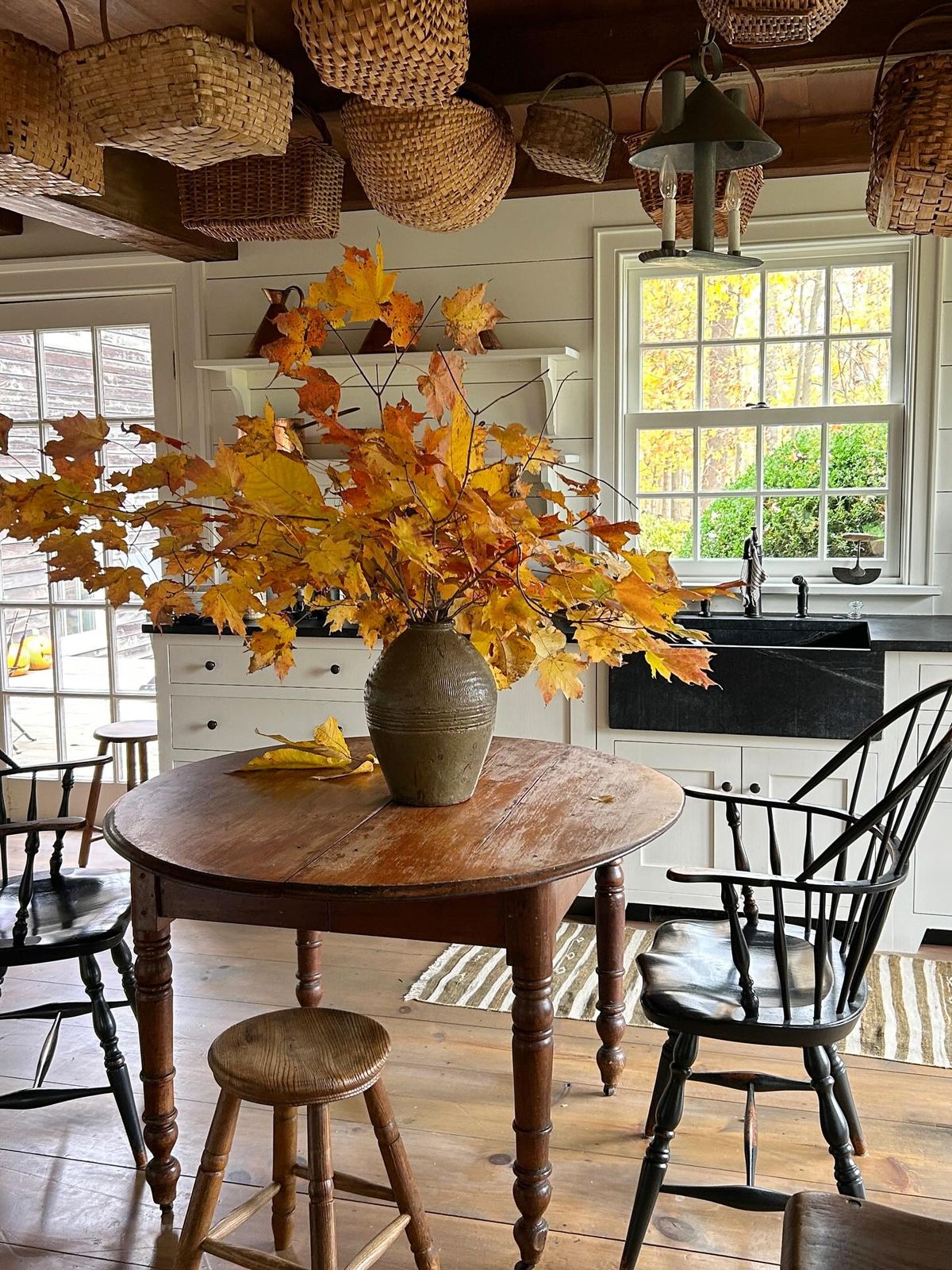Fresh autumn maple leaf branches arranged in a stoneware crock on a rustic kitchen table