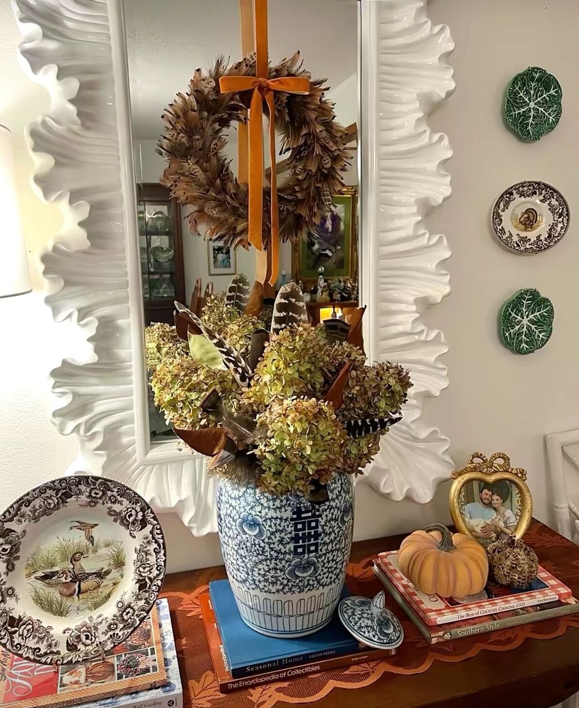 Feather wreath layered over a mirror with a vintage fall vignette below