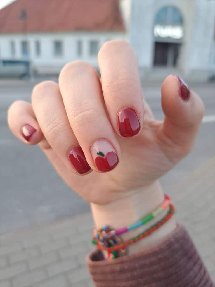Deep red short fall nails with a tiny painted apple accent