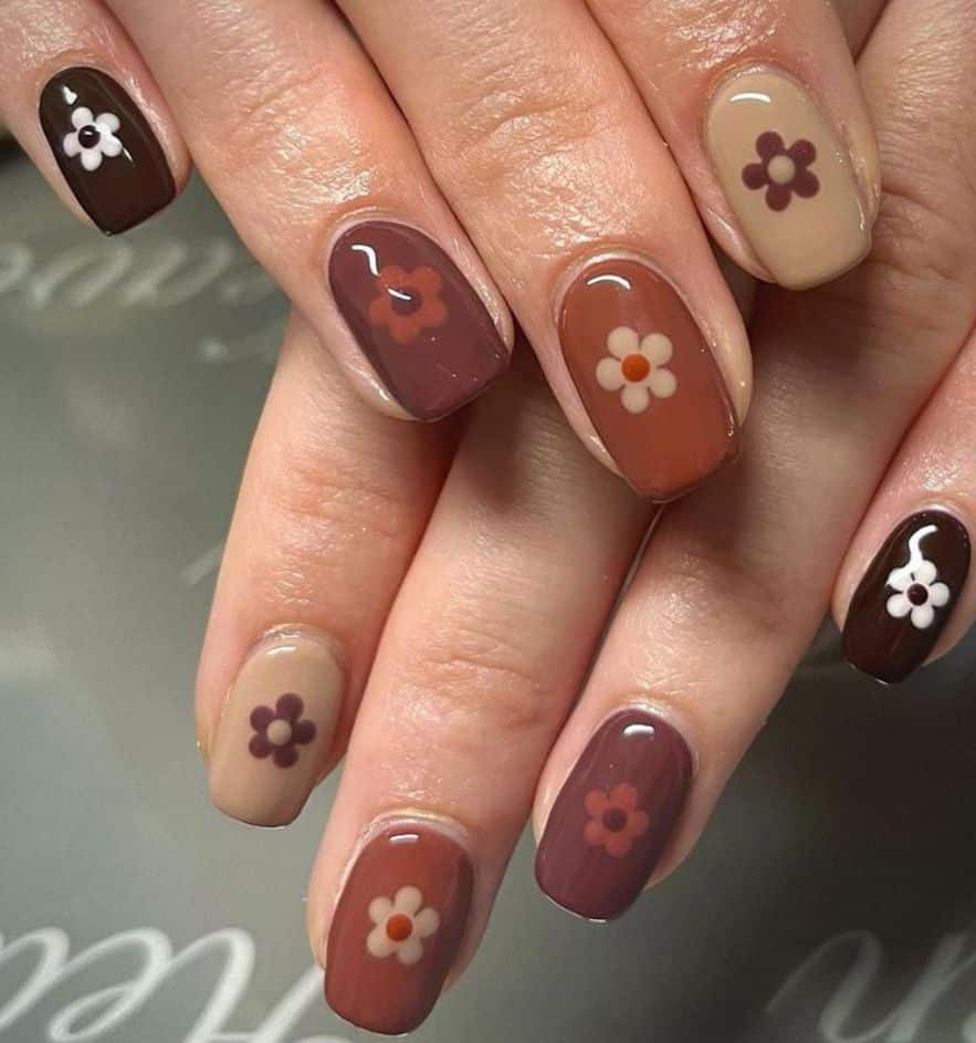 Short squoval fall nails in mixed warm autumn tones each with a retro daisy flower