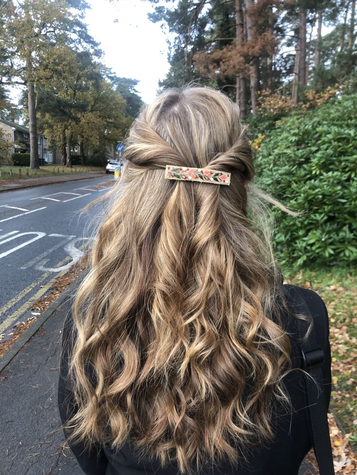 Blonde wavy hair pulled half up and fastened with a floral patterned barrette.