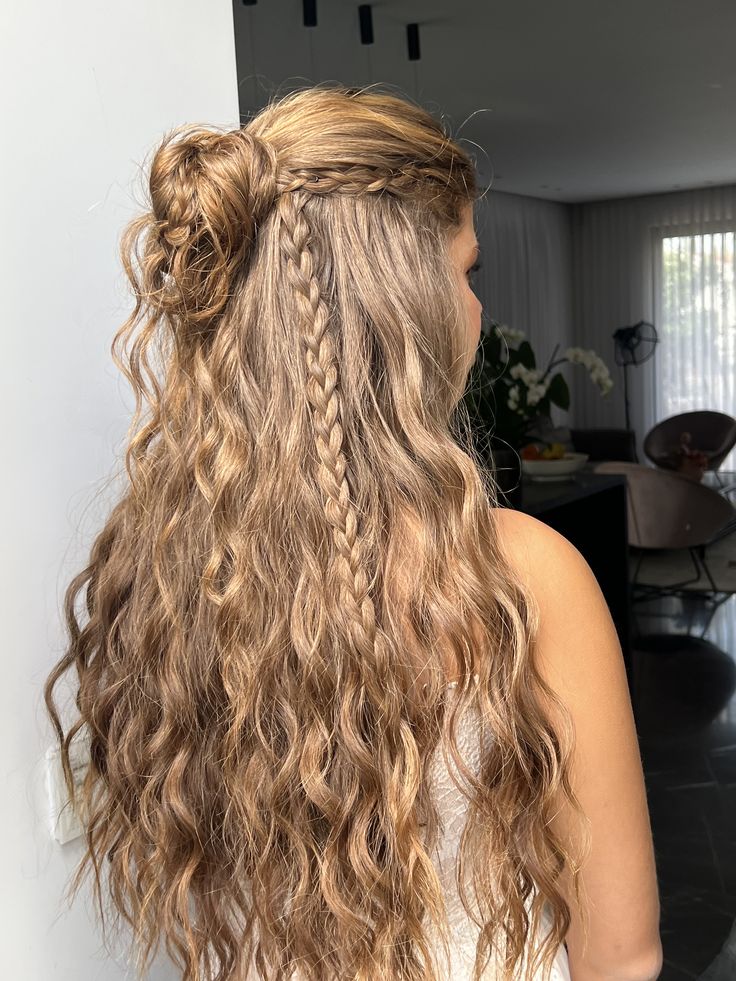 Long curly hair in a half up bun with thin braids woven through the loose length.