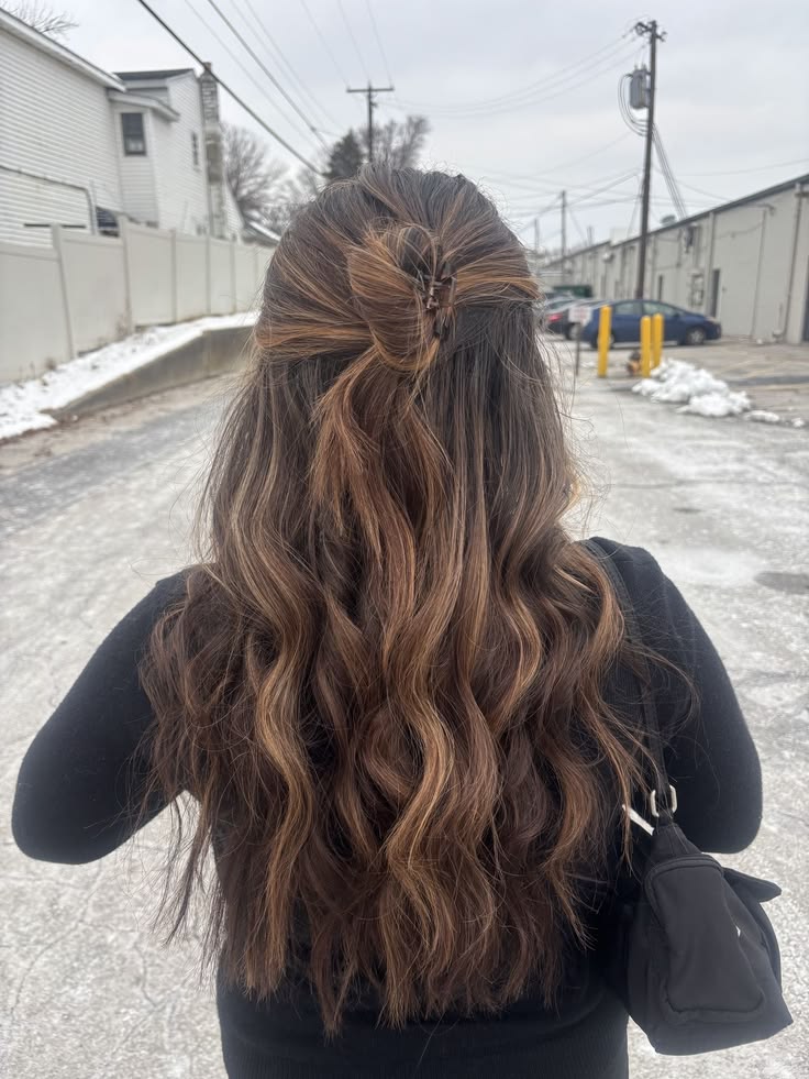 Long wavy brunette hair pulled loosely half up and secured with a small clip.