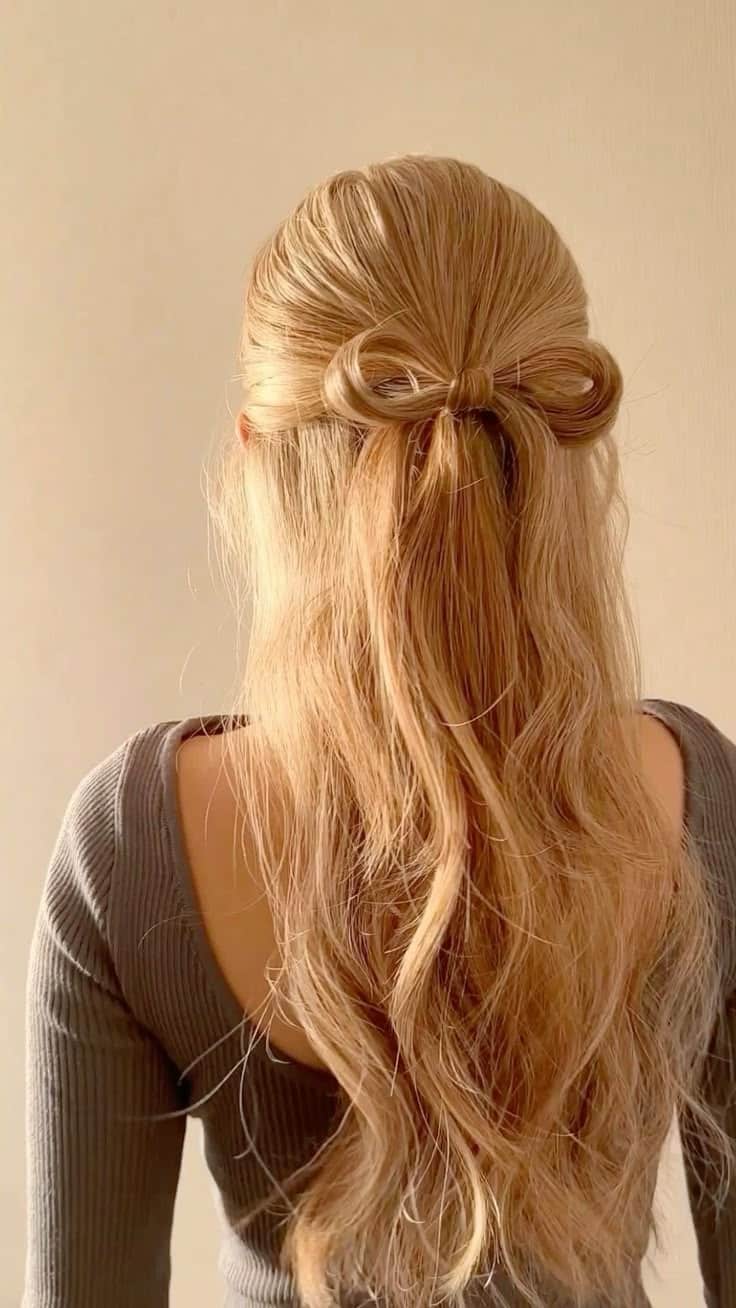 Long blonde hair styled half up with a bow shaped from the hair itself.