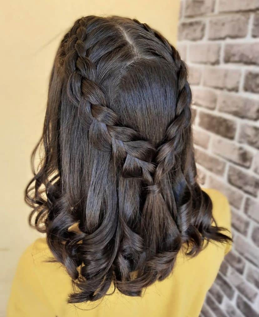 Dark hair in two dutch braids meeting in a half up style with curled ends.