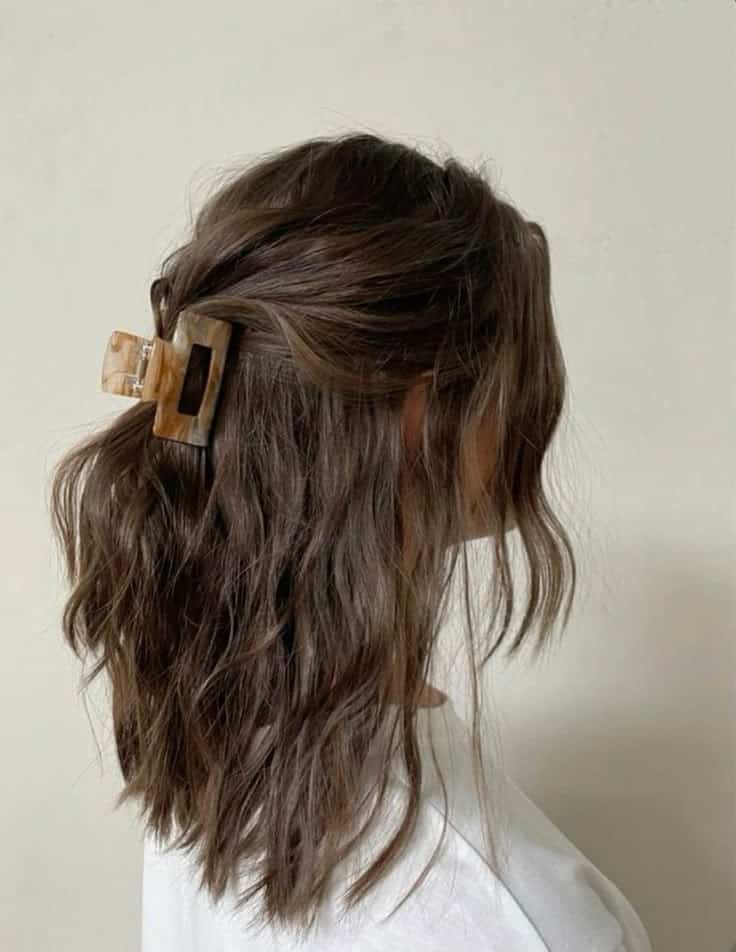 Brown wavy lob twisted into a half up style with a marbled claw clip.
