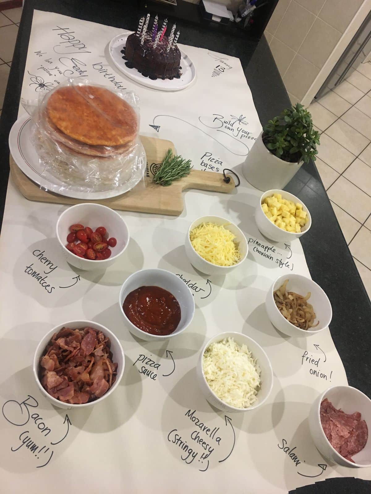 Birthday pizza and topping bar with labelled bowls and a cake at the end