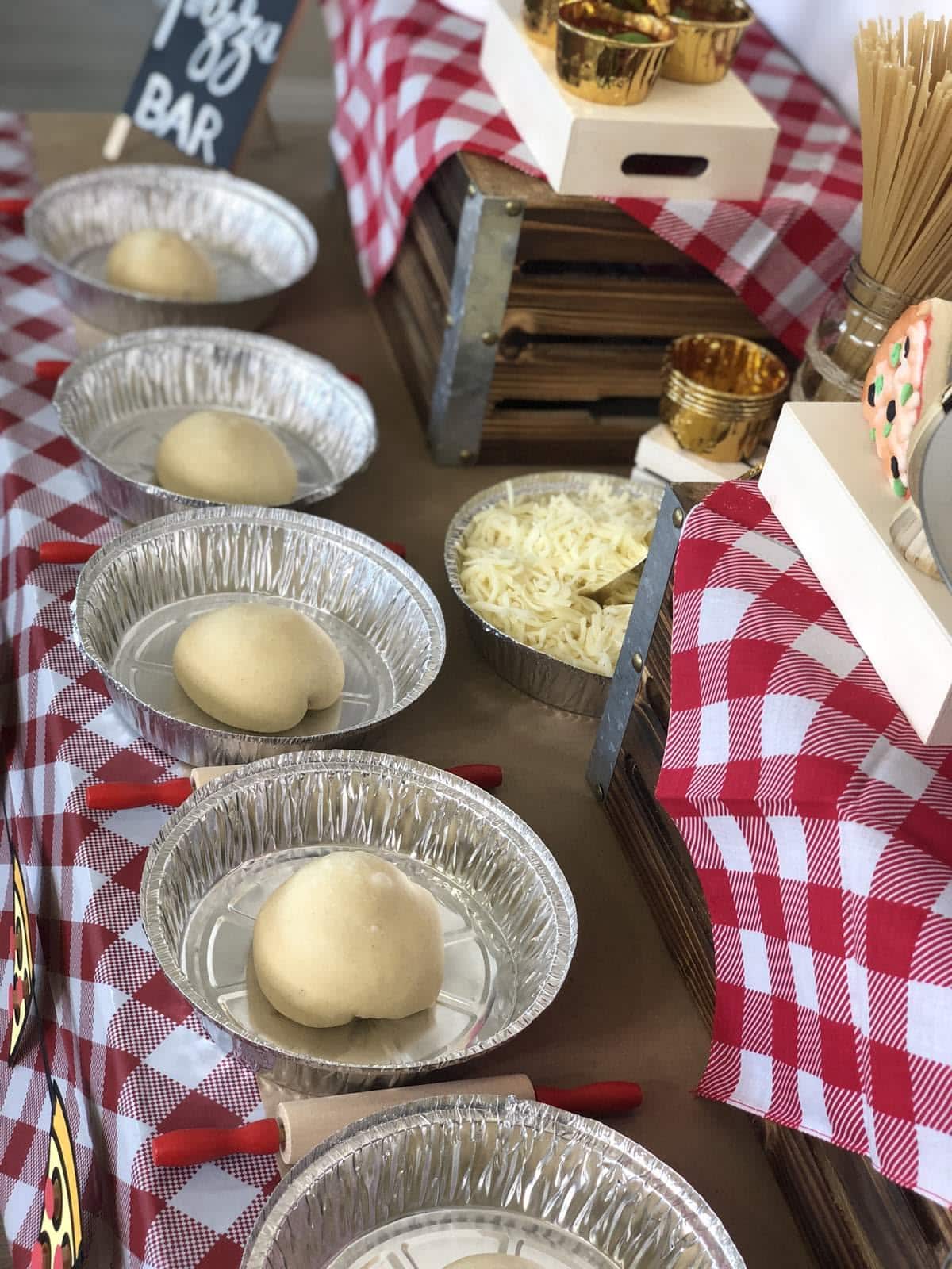 Individual foil pizza pans with dough balls set up for a pizza making party