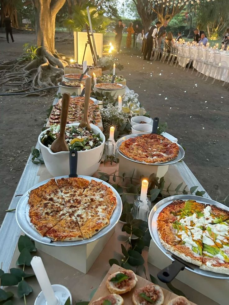 Candlelit pizza table set up outdoors at dusk with string lights in the background