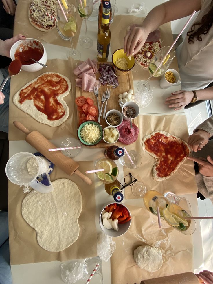 Heart shaped homemade pizzas being topped by a group at a table