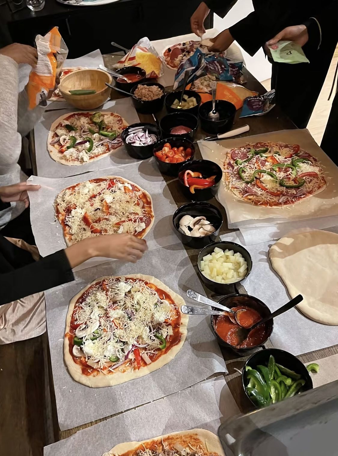 Group of friends topping their own pizzas at a long dinner table
