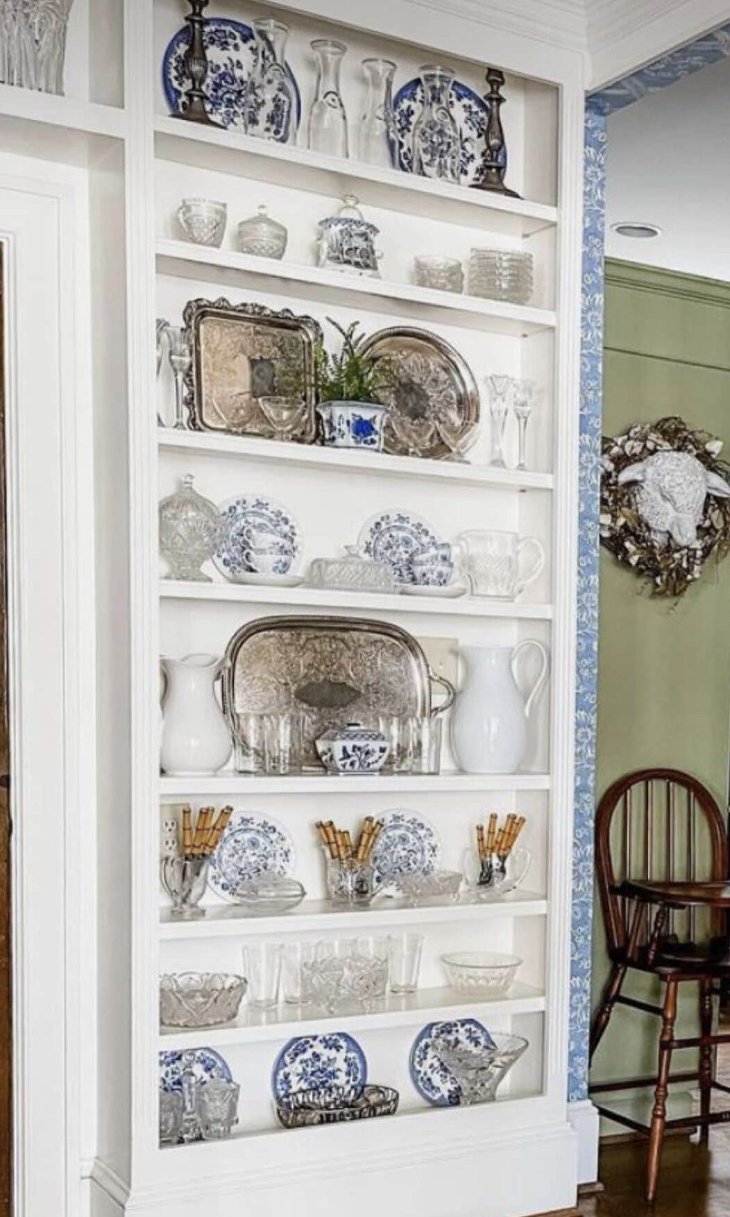 Tall white built-in plate rack wall filled with blue and white china, glassware, and silver trays