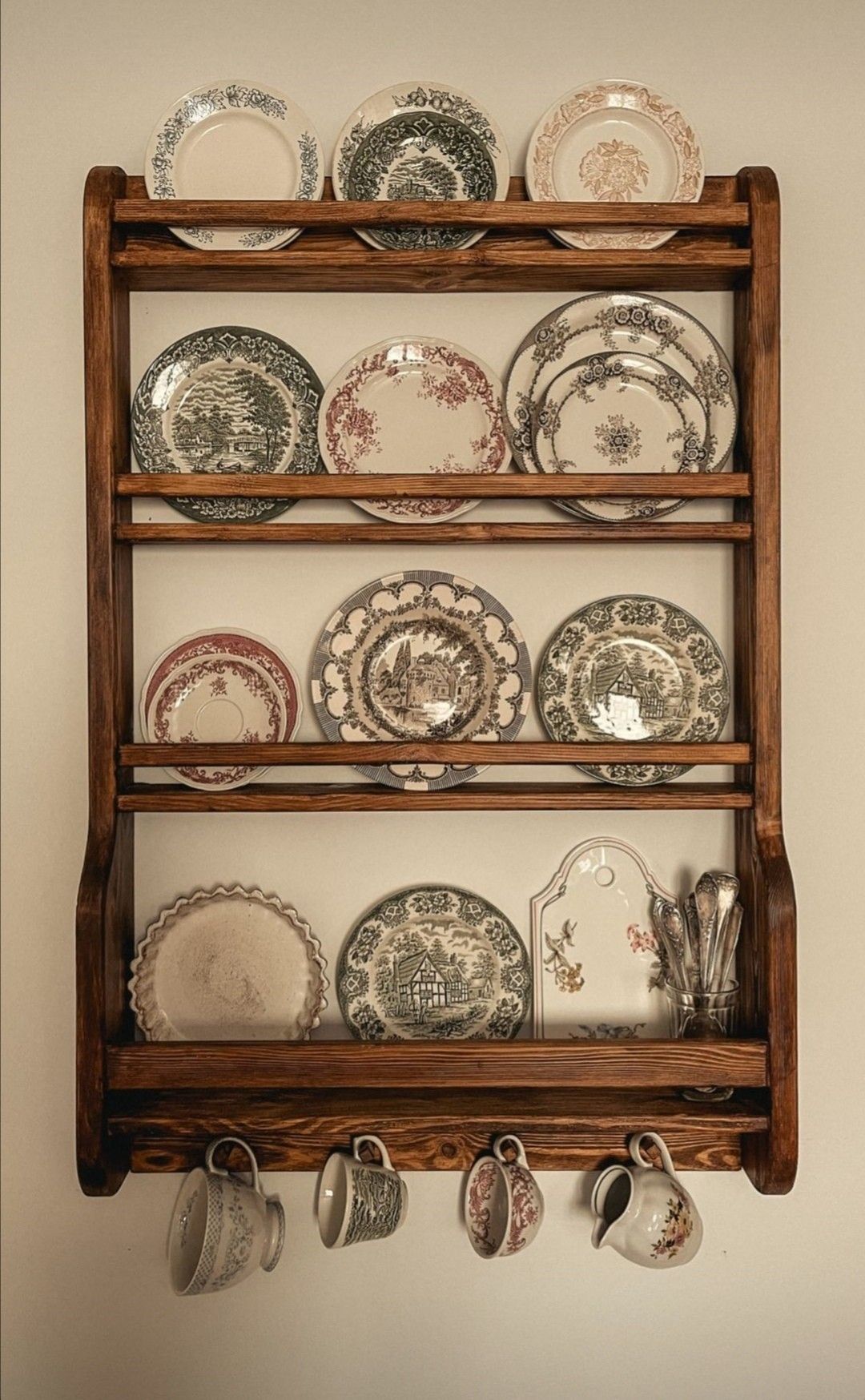Dark wood plate rack displaying mismatched vintage transferware plates with teacups on hooks