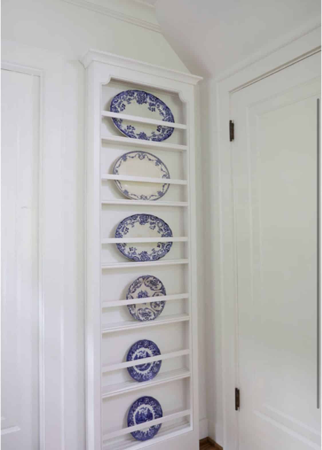Tall narrow white plate rack displaying one blue and white platter on each shelf