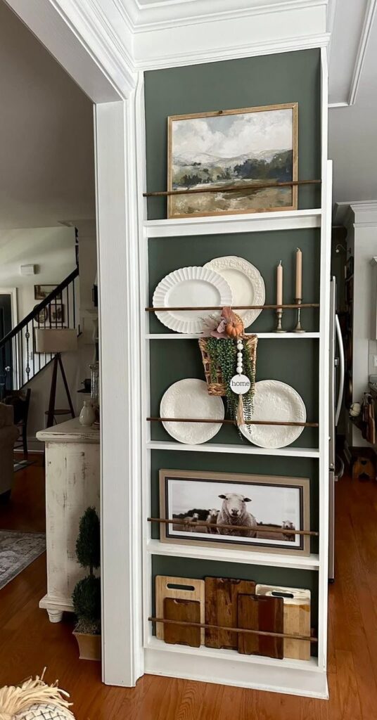 White plate rack ledges on a dark green wall styled with white plates, art, and cutting boards
