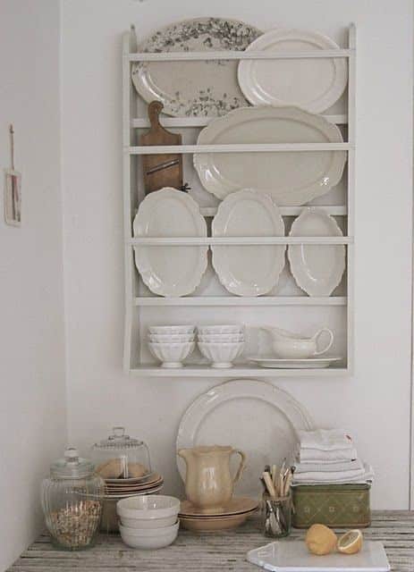 Small white wall mounted plate rack holding vintage cream and white platters