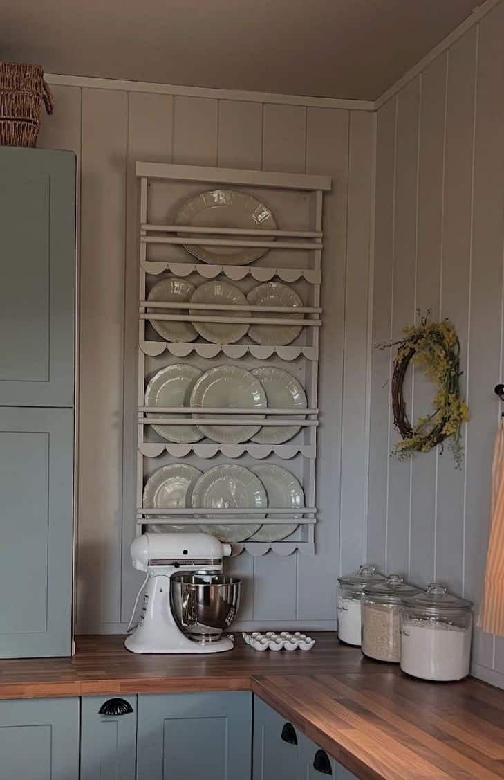 Cream scalloped plate rack wall holding rows of matching cream plates above a kitchen bench