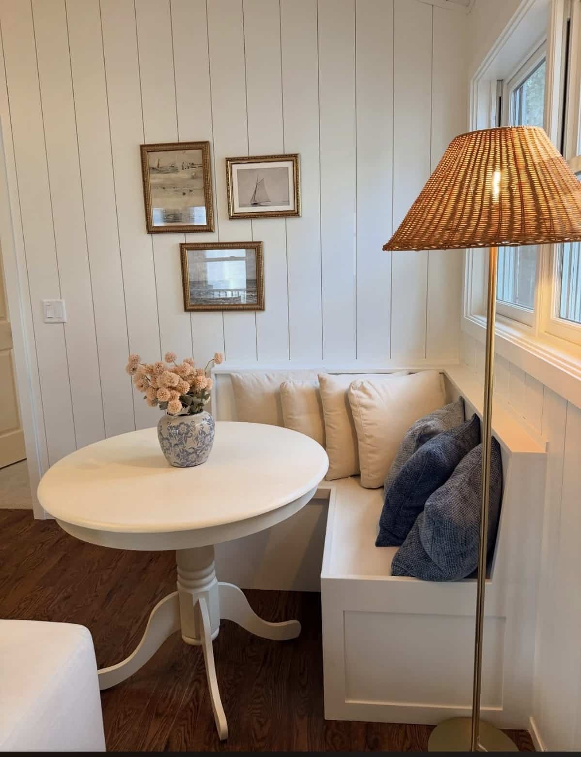 Crisp white built-in corner bench with cream and navy cushions and a round white pedestal table in a coastal kitchen