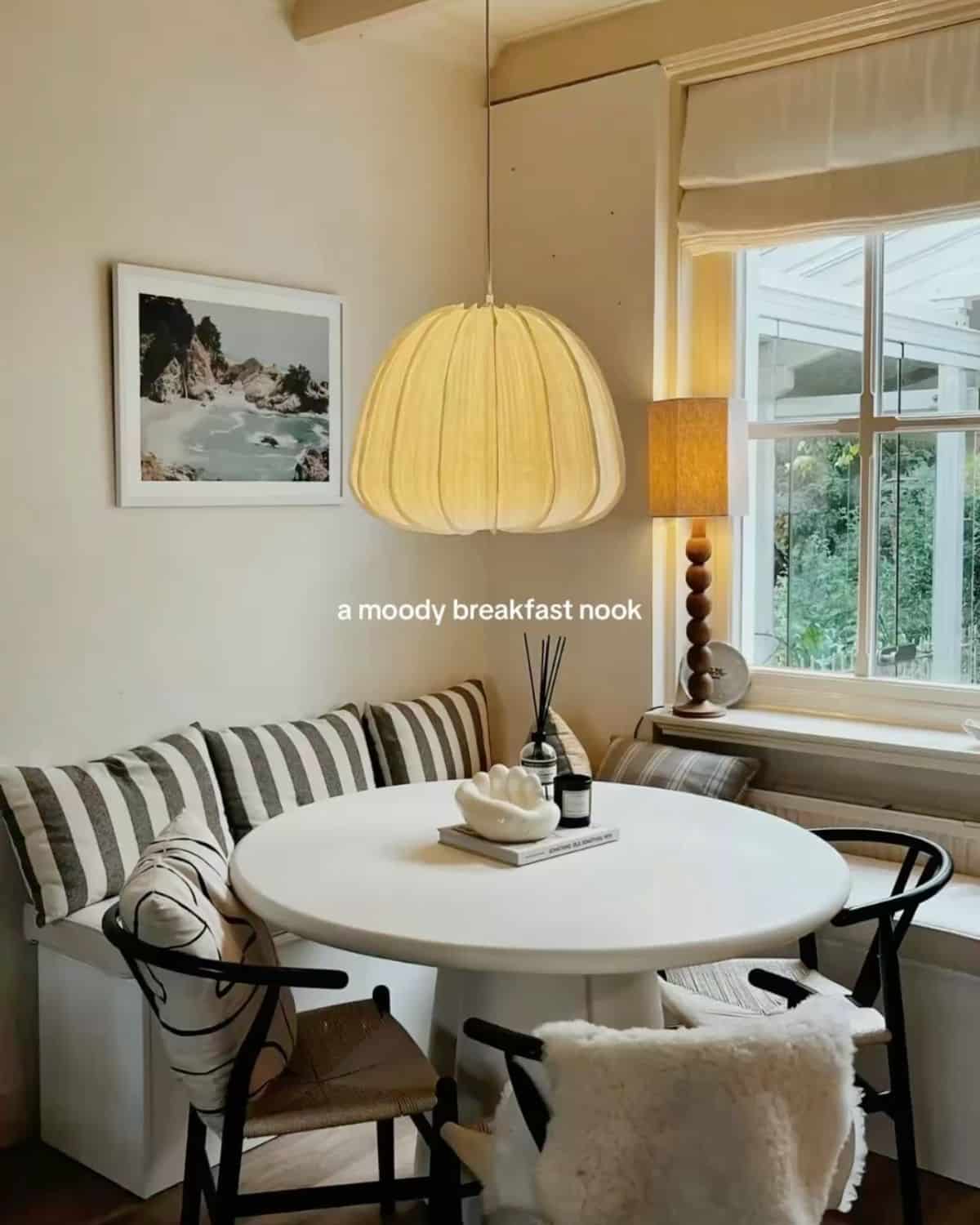 Skirted L-shaped cream banquette with striped pillows paired with black wishbone chairs
