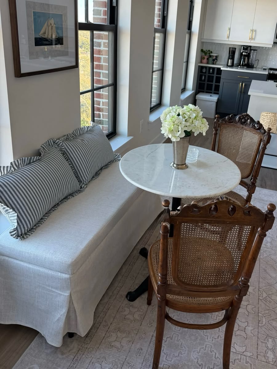Round marble bistro table with a skirted upholstered settee and carved cane antique chairs