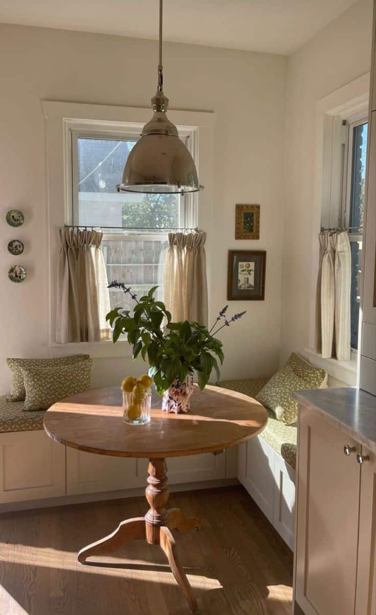 Matching built-in benches on either side of a round pine table below a curtained window