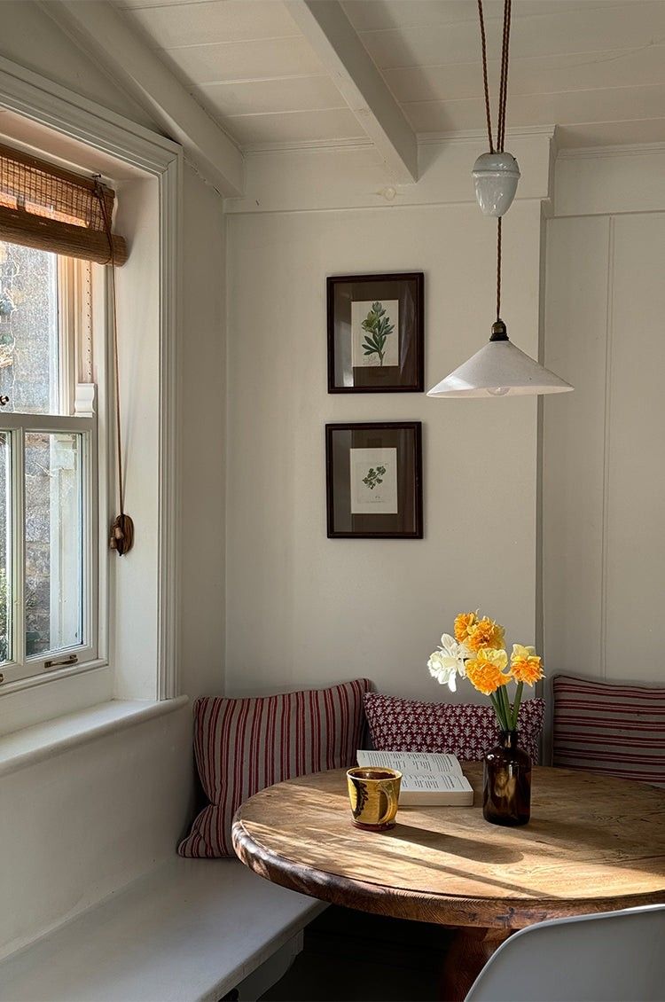 Painted built-in bench with faded red striped cushions and framed botanical prints above