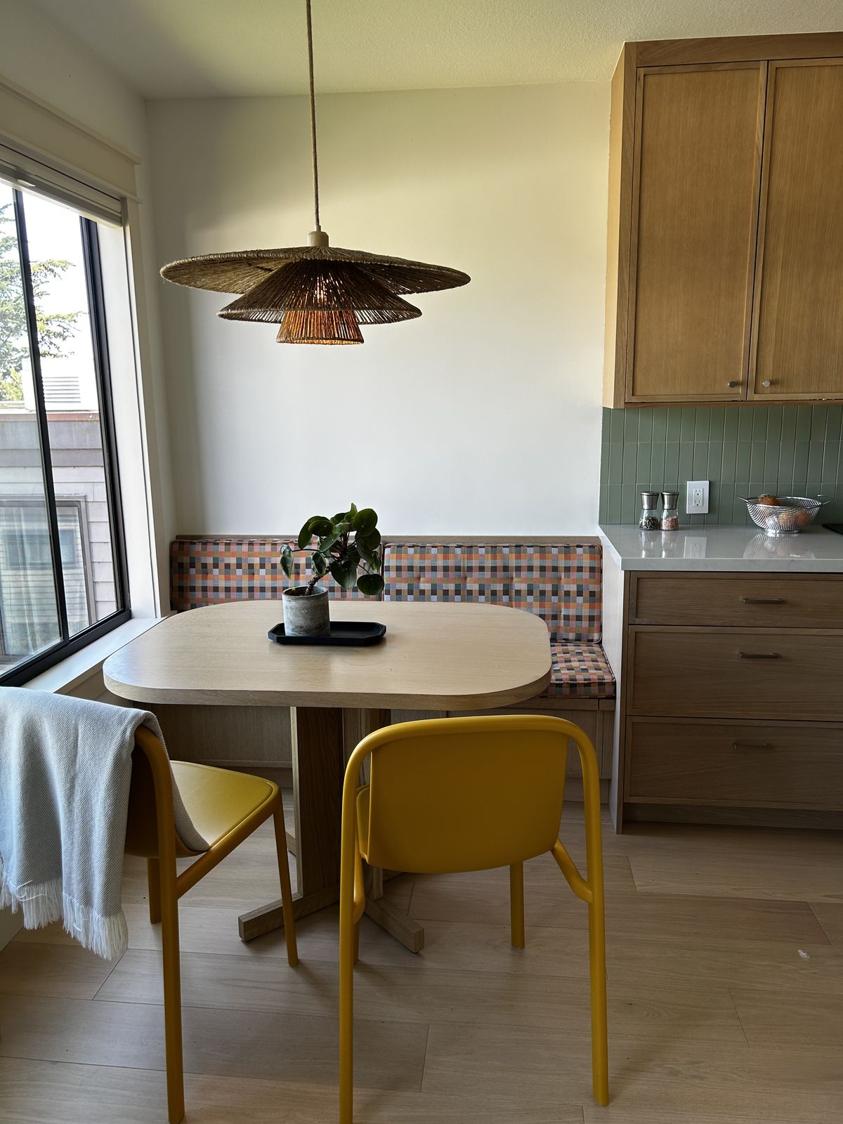 Built-in banquette upholstered in a colourful checkerboard weave with mustard chairs and a rounded oak table