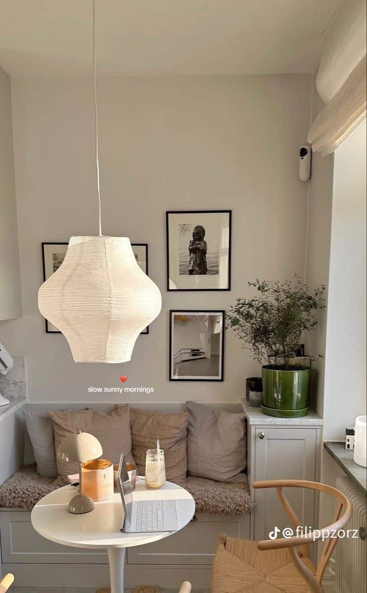 Built-in bench with deep linen cushions below a grid of black-and-white framed photographs beside a round white table and a paper lantern pendant
