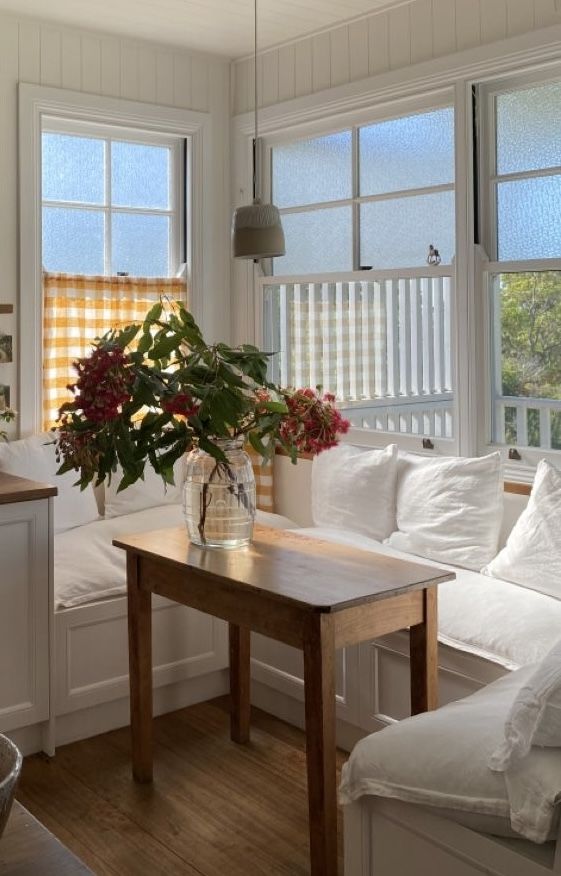 White cushioned window seat with yellow gingham café curtains and a small vintage wooden side table