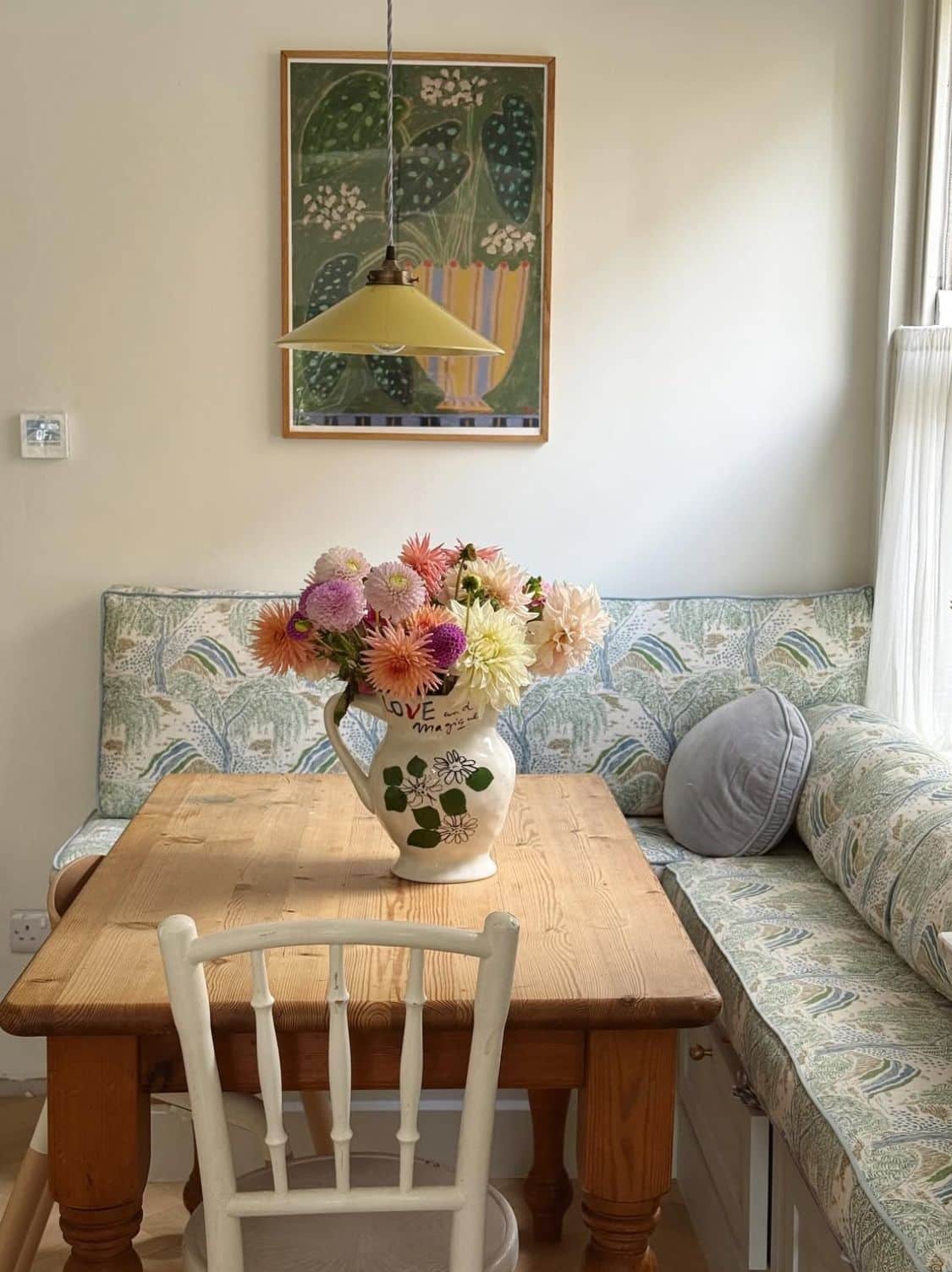 Built-in banquette upholstered in a green botanical print beside a warm pine farmhouse table