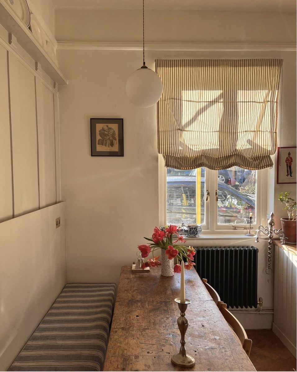 Long upholstered bench with a striped cushion running along a narrow kitchen wall beside a rustic timber table